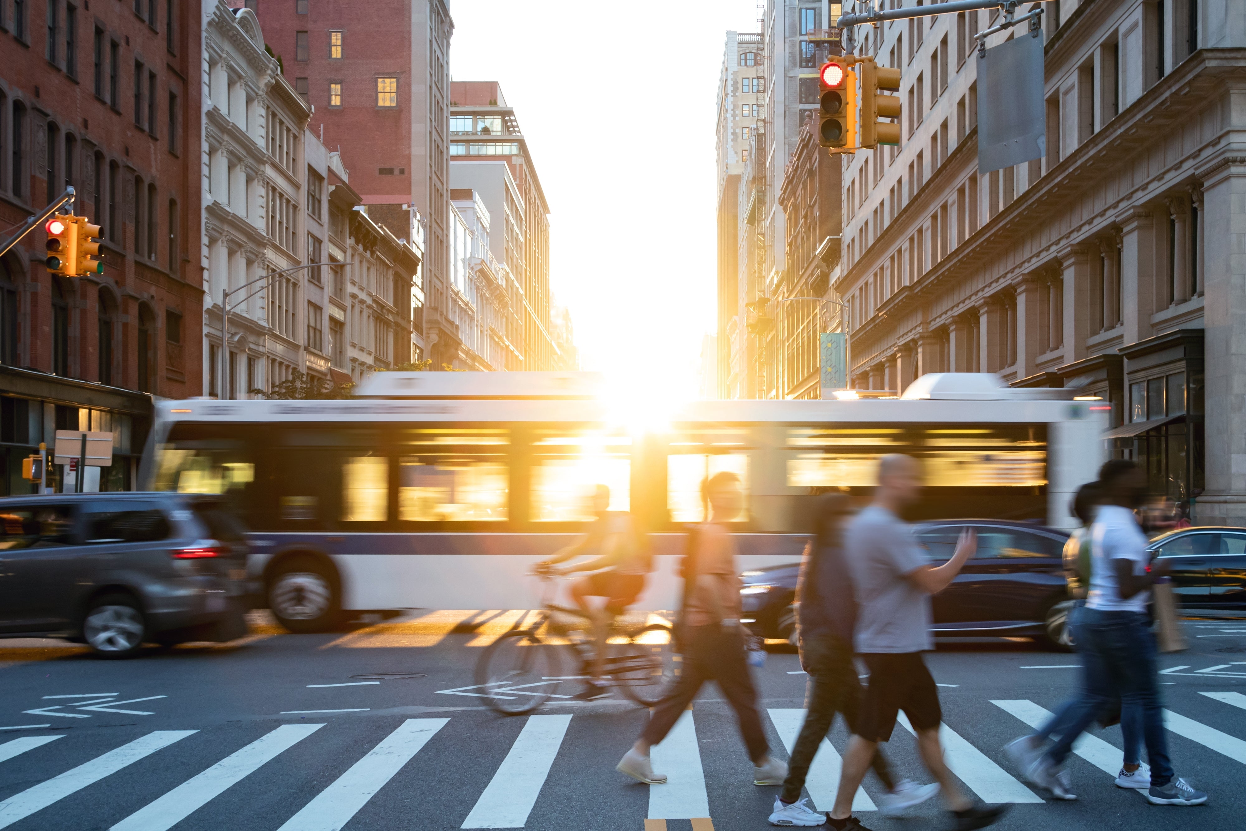 Sun shining through a city bus with cars, bicycles, and pedestrians crossing in front of the camera view