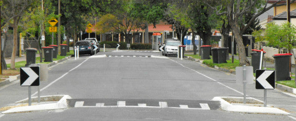 Two lane roadway with raised crosswalks at two locations and cars parked along the roadway