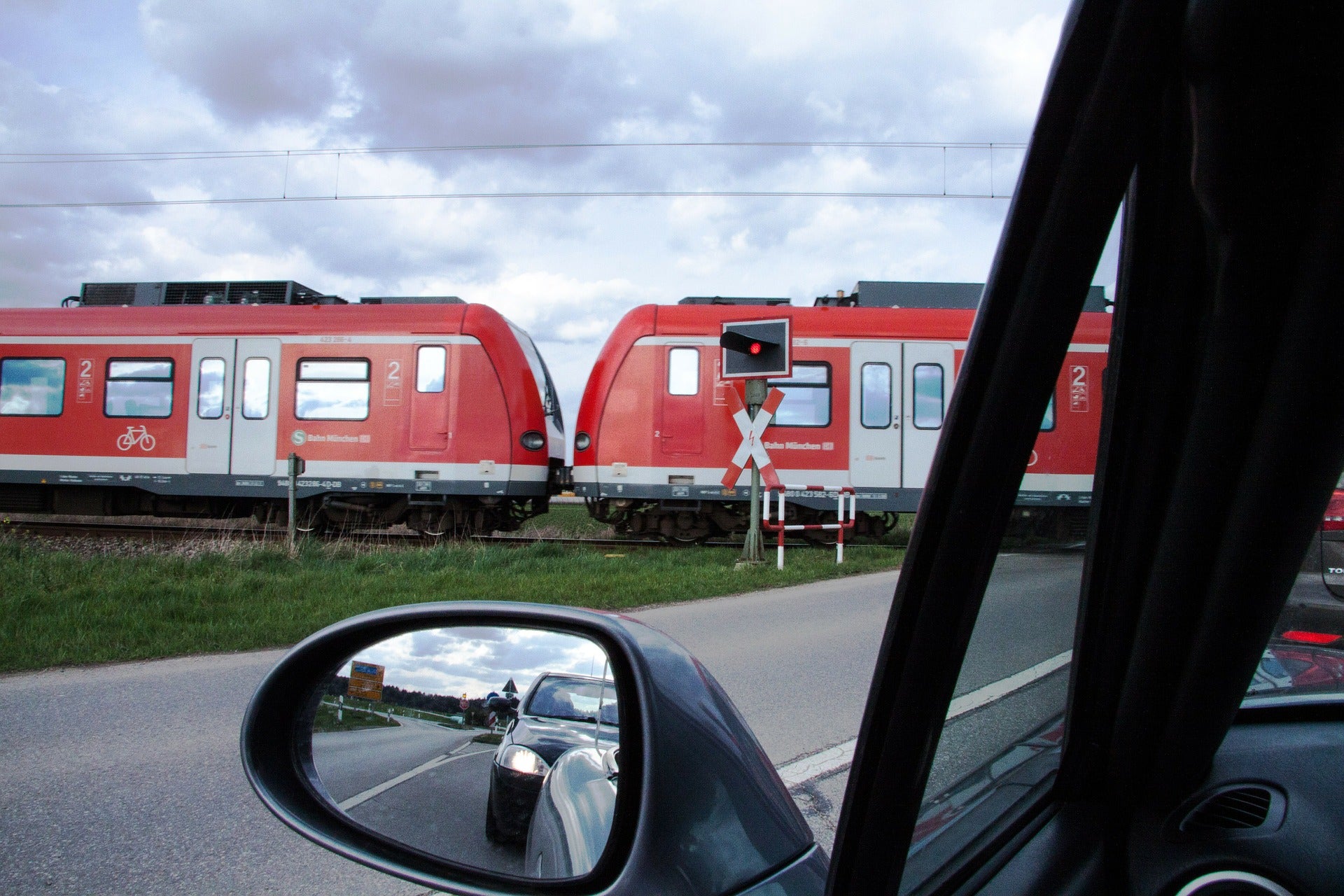 View from the driver side of a car looking at a red and white train crossing an at grade roadway crossing.