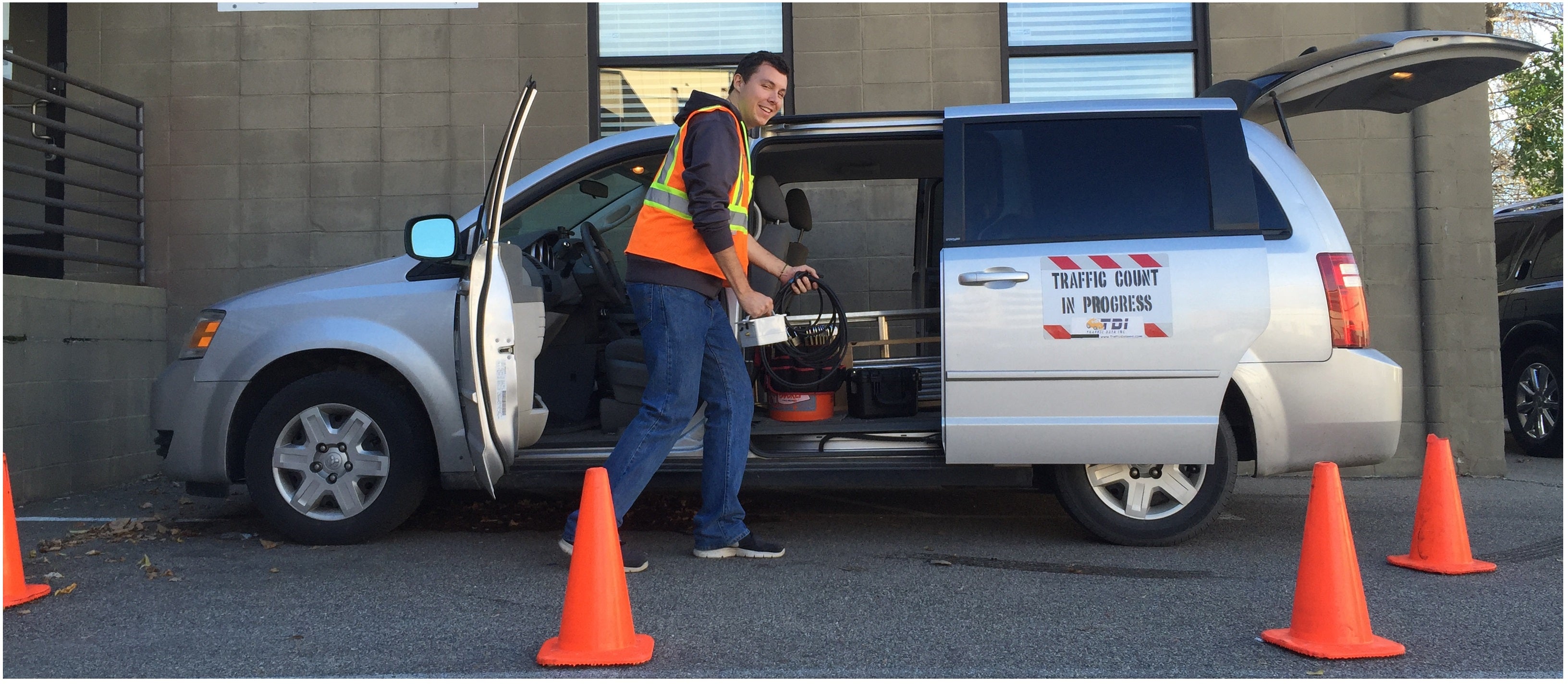 A field worker in an orange safety vest loading a minivan for data collection