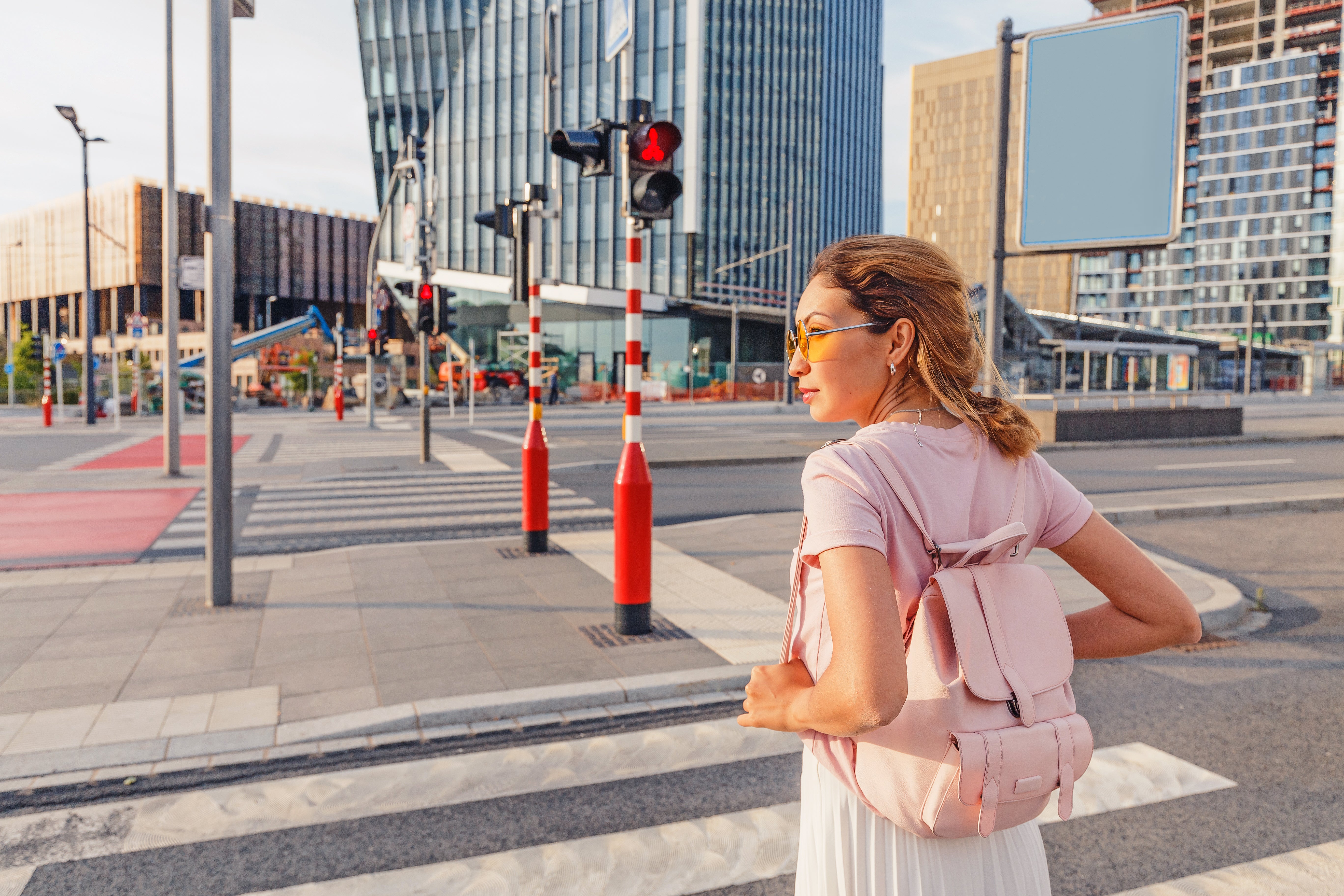 Woman in pink clothes and sunglasses looking for traffic before crossing a roadway in the crosswalk