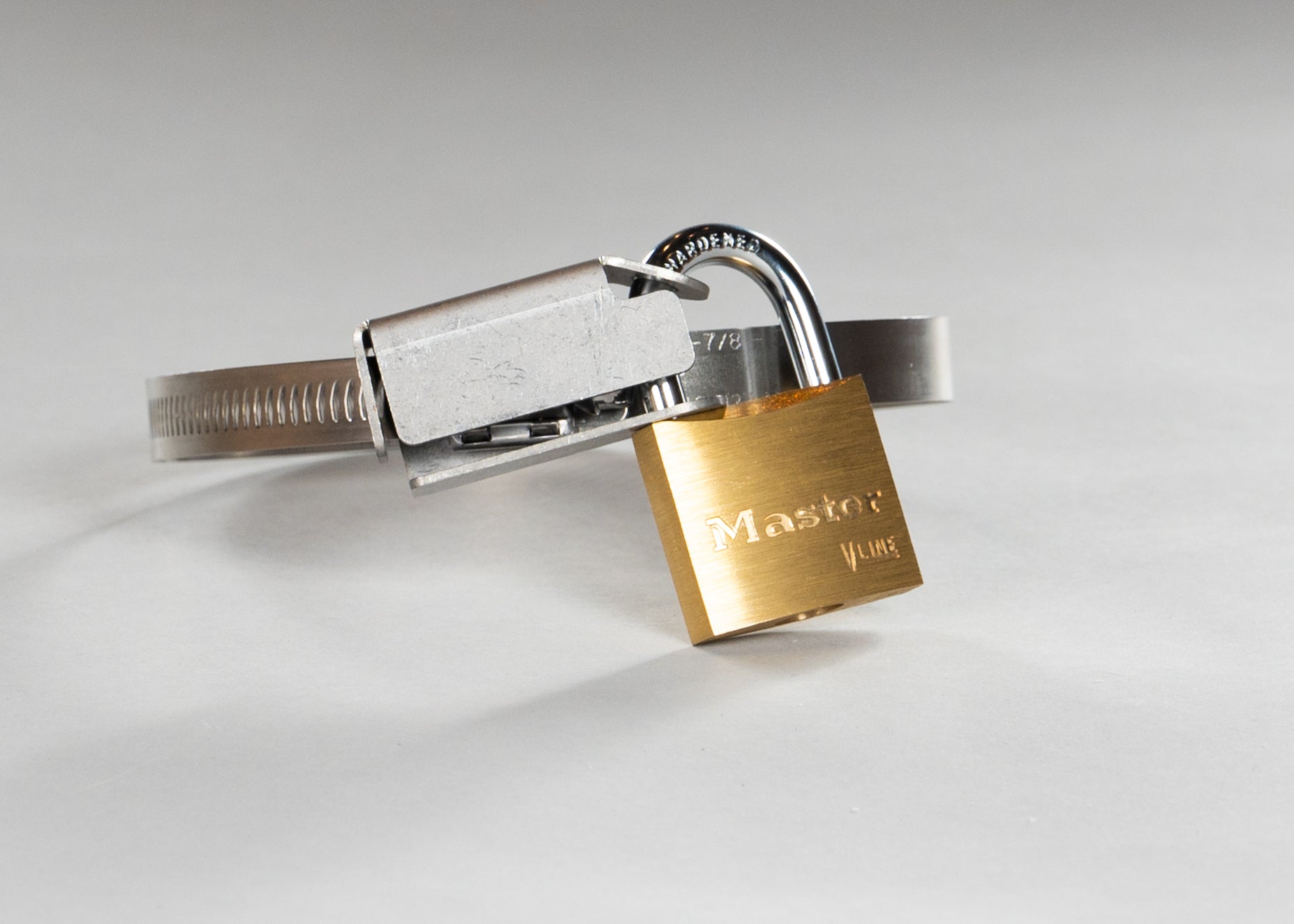 The full hose clamp lock bracket system as used in the field. A gold padlock is installed through the holes of the lock bracket preventing access to the hex driver of the hose clamp